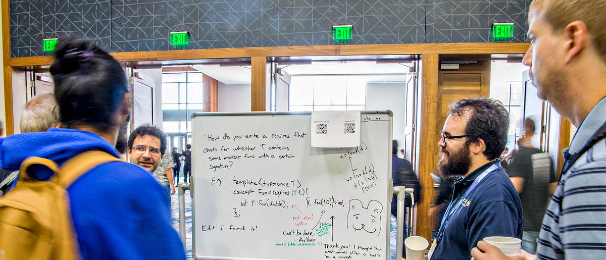 Attendees discussing a C++ concepts whiteboard problem at a CppCon hallway